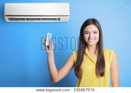 Young woman switching on air conditioner against color background