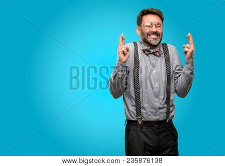 Middle age man, with beard and bow tie with crossed fingers asking for good luck