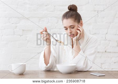 Young Woman With No Appetite, Tired, Bad Mood And Sleepy, Sitting In The White Loft Kitchen, Having 