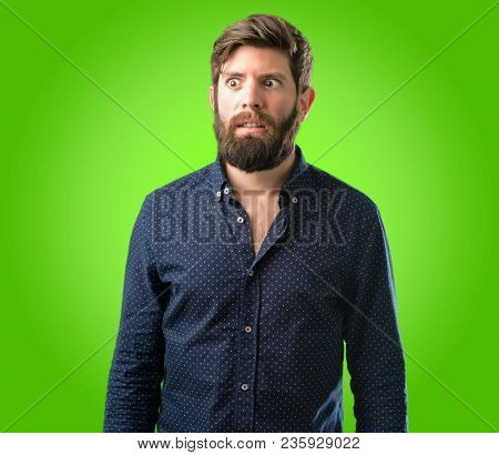 Young hipster man with big beard making funny face fooling over green background