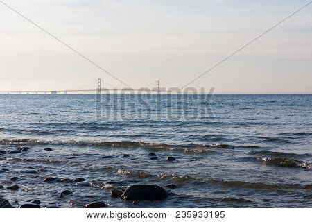 Sunset On The Water With The Mackinac Bridge Viewable In The Distance, And Small Waves Washing Up On