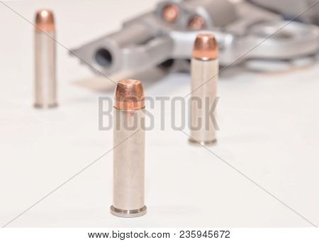 Three .357 Magnum Bullets With A Stainless Loaded Revolver In The Background