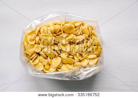 Cornflakes In Plastic Bag On White Wooden Surface. Top View. Place For Your Text