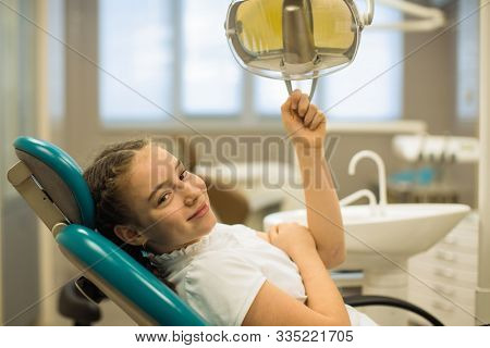 Portrait of a cute happy patient teengirl sitting in a chair in the dental room.
