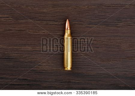 Single Rifle Bullet On Old Wooden Table Close-up.