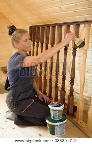 Beautiful Young Woman Painstakingly Paints The Balusters Of The Railing. Construction And Repair.