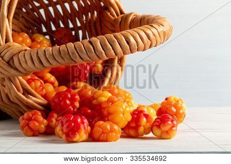 Handful Of Cloudberry Berries Poured From A Small Basket On An White Wooden Table Close-up