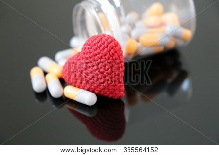 Pills And Knitted Red Heart On Dark Glass Table, Bottle With Medication In Capsules. Concept Of Hype