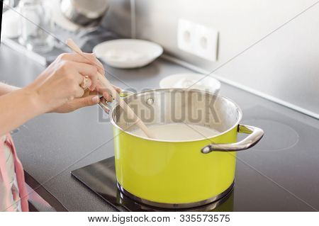 Woman Preparing Bechamel Sauce Or Cream In A Pan. Woman Hand Is Mixing Boiling Milk With Wooden Spoo
