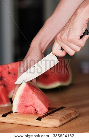 Hands Chop Watermelon With A Knife On A Bamboo Cutting Board. Side View