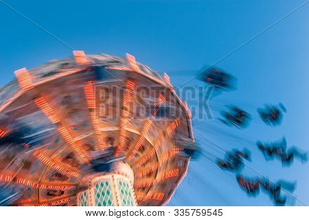 Amusement Park Motion Blurred Riders On Retro Vintage Tilting Swing Against Clear Blue Sky.