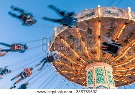Amusement Park Motion Blurred Riders On Retro Vintage Tilting Swing Against Clear Blue Sky.