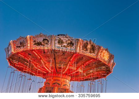 Brightly Red Lit Amusement Park Twirling Swing Ride With Chains, In A Stopped Position Against A Blu