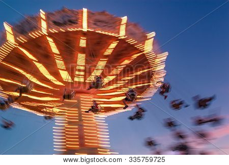 Amusement Park Motion Blurred Riders On Brightly Lit Retro Vintage Tilting Swing At Blue Hour.