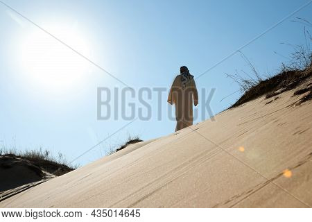 Man In Arabic Clothes Walking Through Desert On Sunny Day, Back View