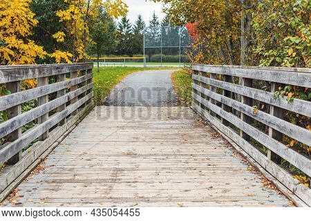 Autumn Scenery In Local Public Park. Old Wooden Bridge And Trees With Fallen Colored Leaves In The B