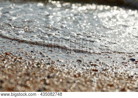 Tidal Bore. The Wave Rolls Onto The Seashore, Which Is Covered With Shells. Coastline. Sea Waves Wit