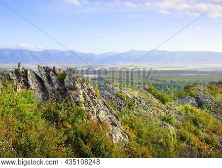 Sharp Rocks On The Top Of A Mountain Above A Mountain Valley Under A Blue Cloudy Sky. Siberia, Russi