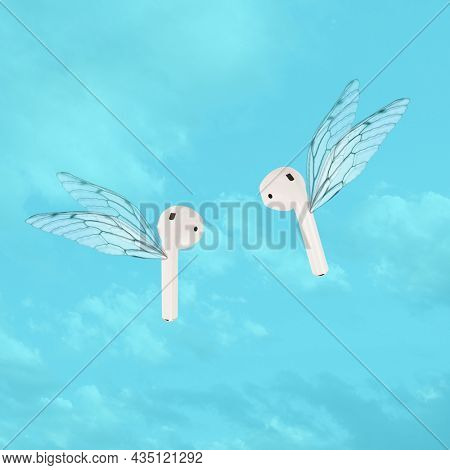 Modern wireless ear phones flying with wings. Sound listening concept photo. In ear headphones. Trendy minimal composition with blue sky background