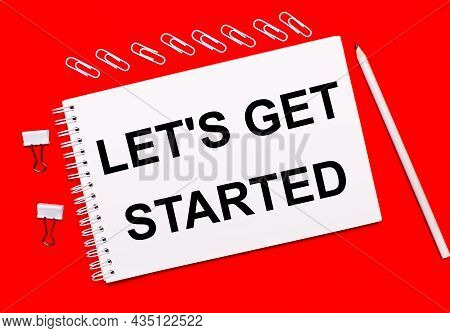 On A Bright Red Background, A White Pencil, White Paper Clips, And A White Notebook With The Text Le