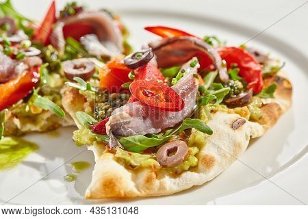 Tapas with avocado cream, anchovy, paprika and kalamata olives on focaccia. Bruschetta with guacamole and anchovy isolated on white background. Appetizer contemporary concept. Fish antipasti