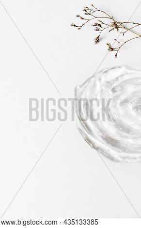 Gel Texture Of The Emulsion On A White Background. Transparent Cream, Small Dry Flowers And Copy Spa