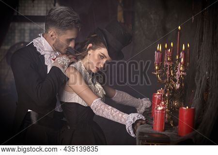 Attractive noble vampire in medieval dress is going to bite a beautiful young lady in his old castle. Halloween. Vampires.