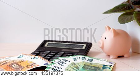 A Piggy Bank, A Calculator And Paper Money In Denominations Of 100 And 50 Euros, Spread Out In A Fan
