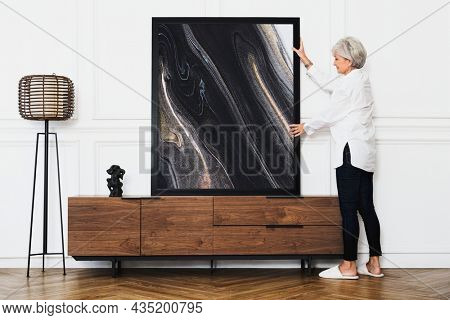 Senior woman adjusting an aesthetic photo frame on a wooden cabinet in a Japandi living room