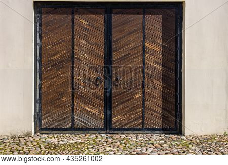 Large Vintage Wooden Gate Wrought Iron In A Light Stone Wall. There Is An Old Stone Pavement In Fron