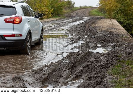 Clean White Suv Car Moving On Dirt Road With Wet Clay In Front Of Blurry Slope At Autumnal Cloudy Da