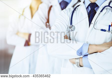 Group Of Modern Doctors Standing As A Team With Crossed Arms And Stethoscopes In A Sunny Hospital Of