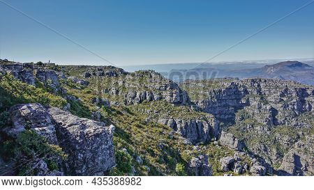 A Tiny Silhouette Of A Man Is Visible On The Flat Top Of Table Mountain. There Is Scant Vegetation O