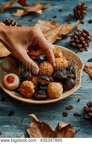 a young man takes a panellet, a typical confection of Catalonia, Spain, eaten traditionally in All Saints Day, from a plate with some more and a roasted sweet potato and some roasted chestnuts