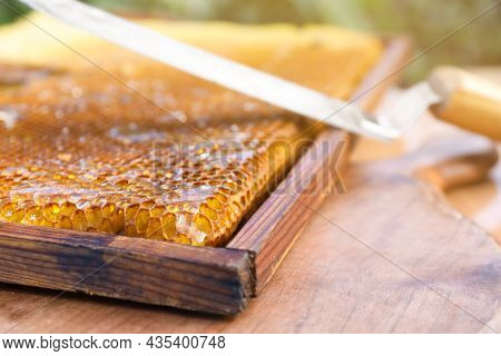 Uncapping Knife And Honeycomb Frame On Wooden Table Outdoors, Closeup
