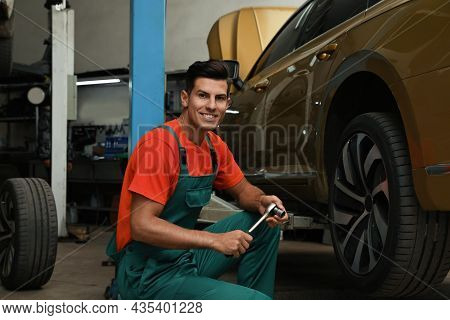 Portrait Of Professional Mechanic With Tire Wrench Near Car At Automobile Repair Shop