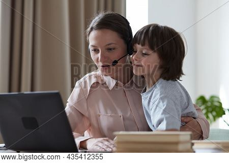 Young Female Tutor Working And Learning Remotely From Home On Video Conference When Son Rushes Up