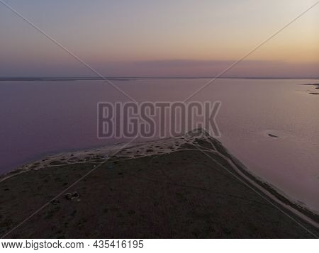 Aerial Drone Shot Of Colorful Pink Lake At Sunset Time With Wind Turbines Farm On Background. Cinema