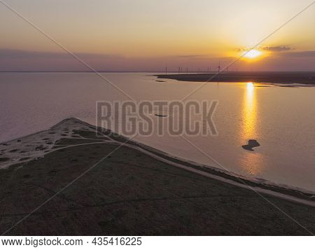 Aerial Drone Shot Of Colorful Pink Lake At Sunset Time With Wind Turbines Farm On Background. Cinema