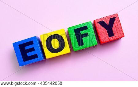 On A Light Pink Background, Multi-colored Wooden Cubes With The Text Eofy.
