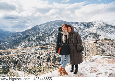 Winter Portrait Of Hugging And Smiling Mother And Daughter With Splendid Snow-covered Mountains View