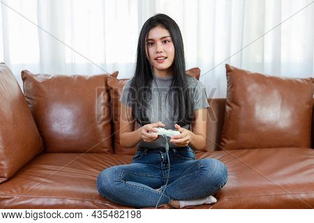 Vdo Game Console Station Concept. Active Asian Woman Sitting On Sofa, Holding Joystick And Playing E