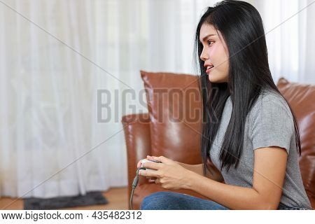 Vdo Game Console Station Concept. Active Asian Woman Sitting On Sofa, Holding Joystick And Playing E
