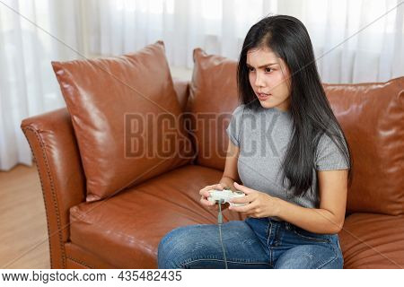 Vdo Game Console Station Concept. Active Asian Woman Sitting On Sofa, Holding Joystick And Playing E