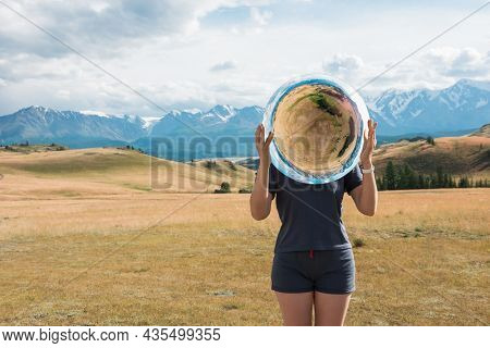 Woman standing in in summer Altai mountains in Kurai steppe and holding circle mirror. 360 aerial panorama of Kurai steppe in mirror. Creative travel concept