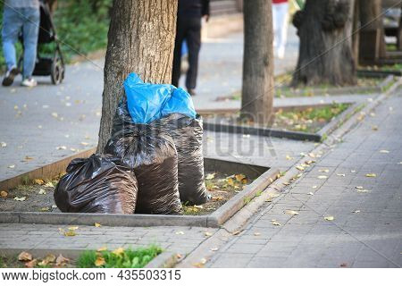 Pile Of Black Garbage Bags Full Of Litter Left For Pick Up On Street Side. Trash Disposal Concept.