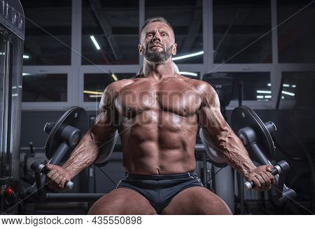 Image Of A Powerful Athlete Sitting On A Bench In A Gym And Pumping Biceps. Fitness And Bodybuilding