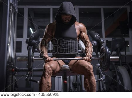 Image Of A Powerful Athlete In A Hoodie Sitting On A Bench In A Gym. Fitness And Bodybuilding Concep