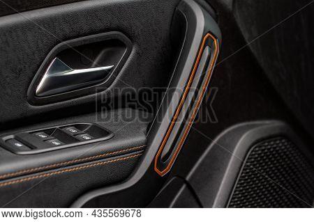 Car Door Handle With Power Window Control. Dark Leather Interior Of Modern Car. Dark Black And Orang