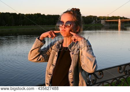 Young Pretty Girl In Sun Glasses With Backpack Walks Along  Embankment Of City In Rays Of Sunset.  C
